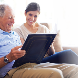 Older adult man and young woman sitting on sofa together looking at photo albums